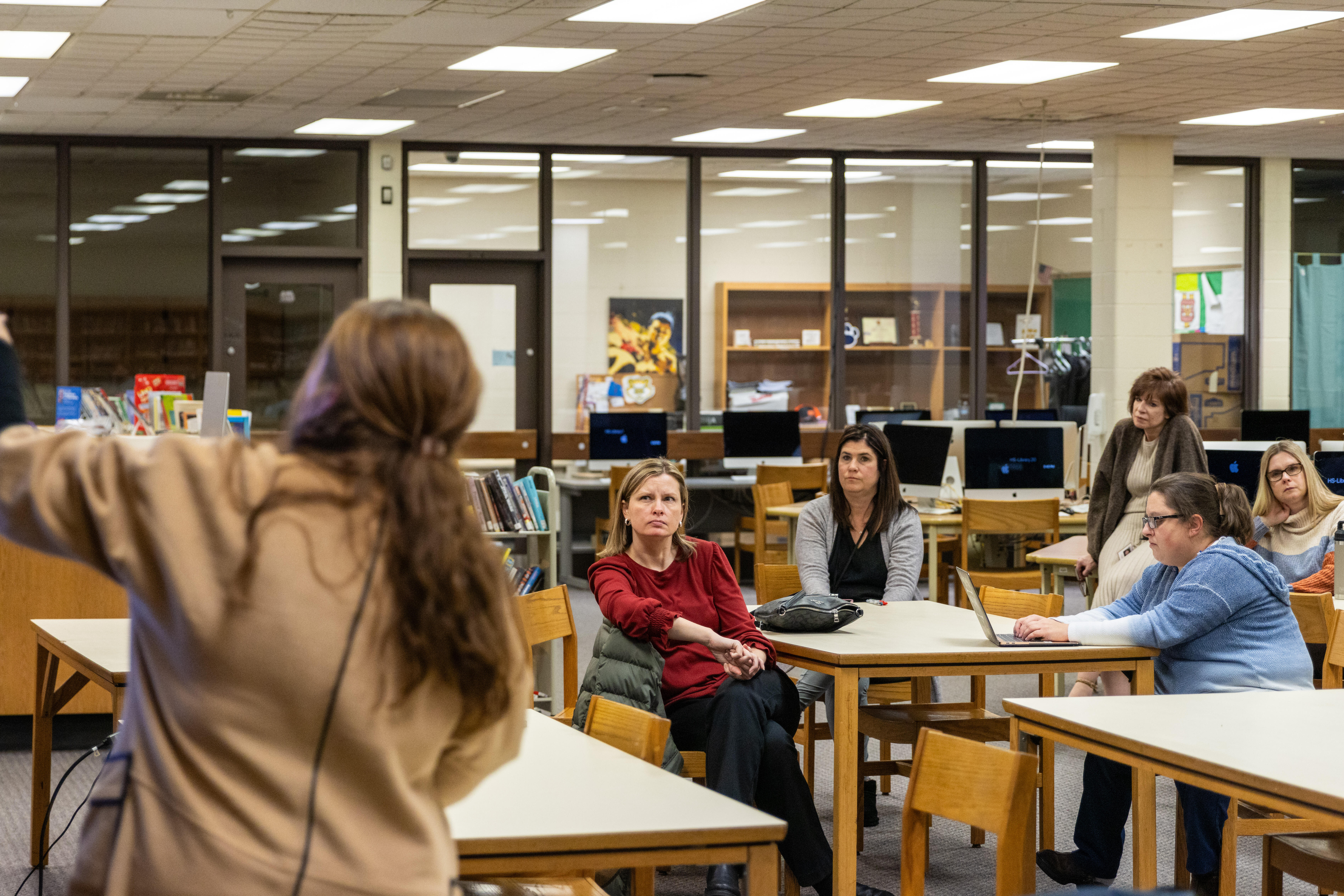 A woman stands at a digital screen and gestures while talking to an audience in a school library