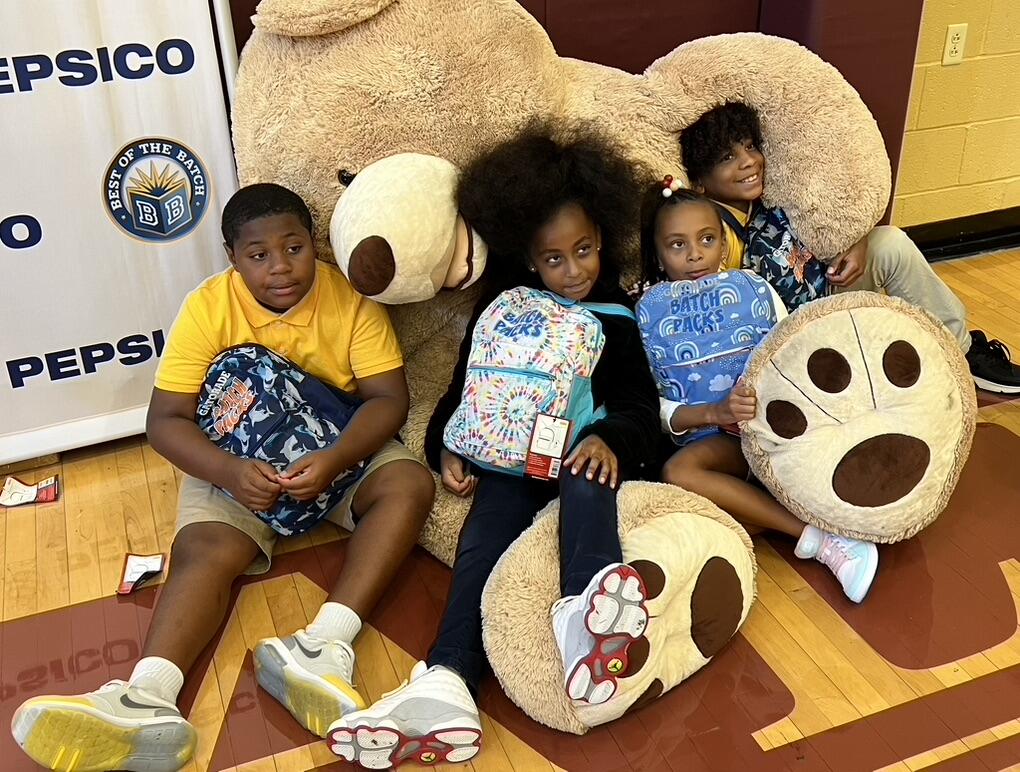 Barrett students show off their new back packs while sitting in a large stuffed bear