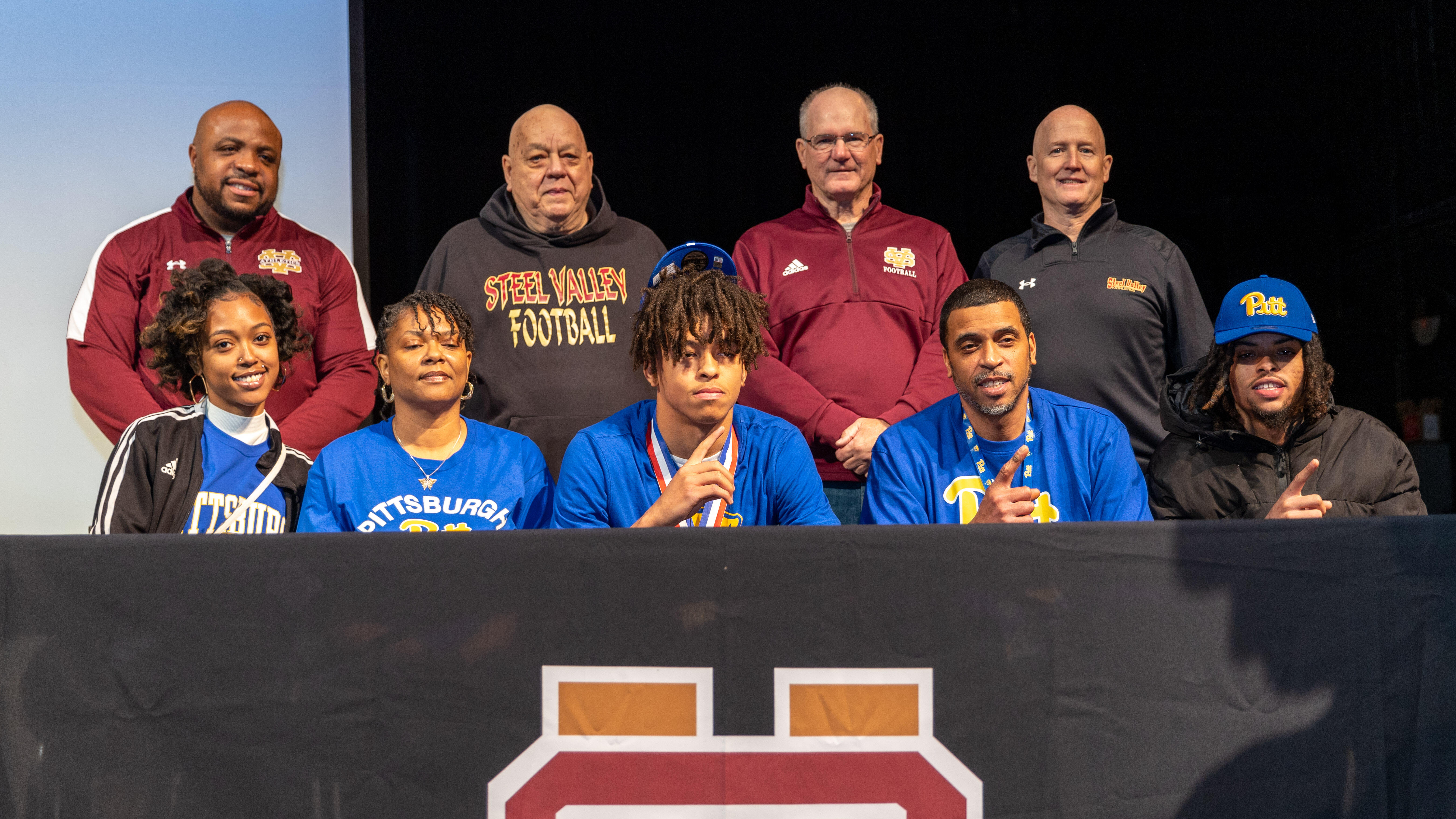 Cruce Brookins poses for a photo with his family and coaches. He is seated at a table on a stage.