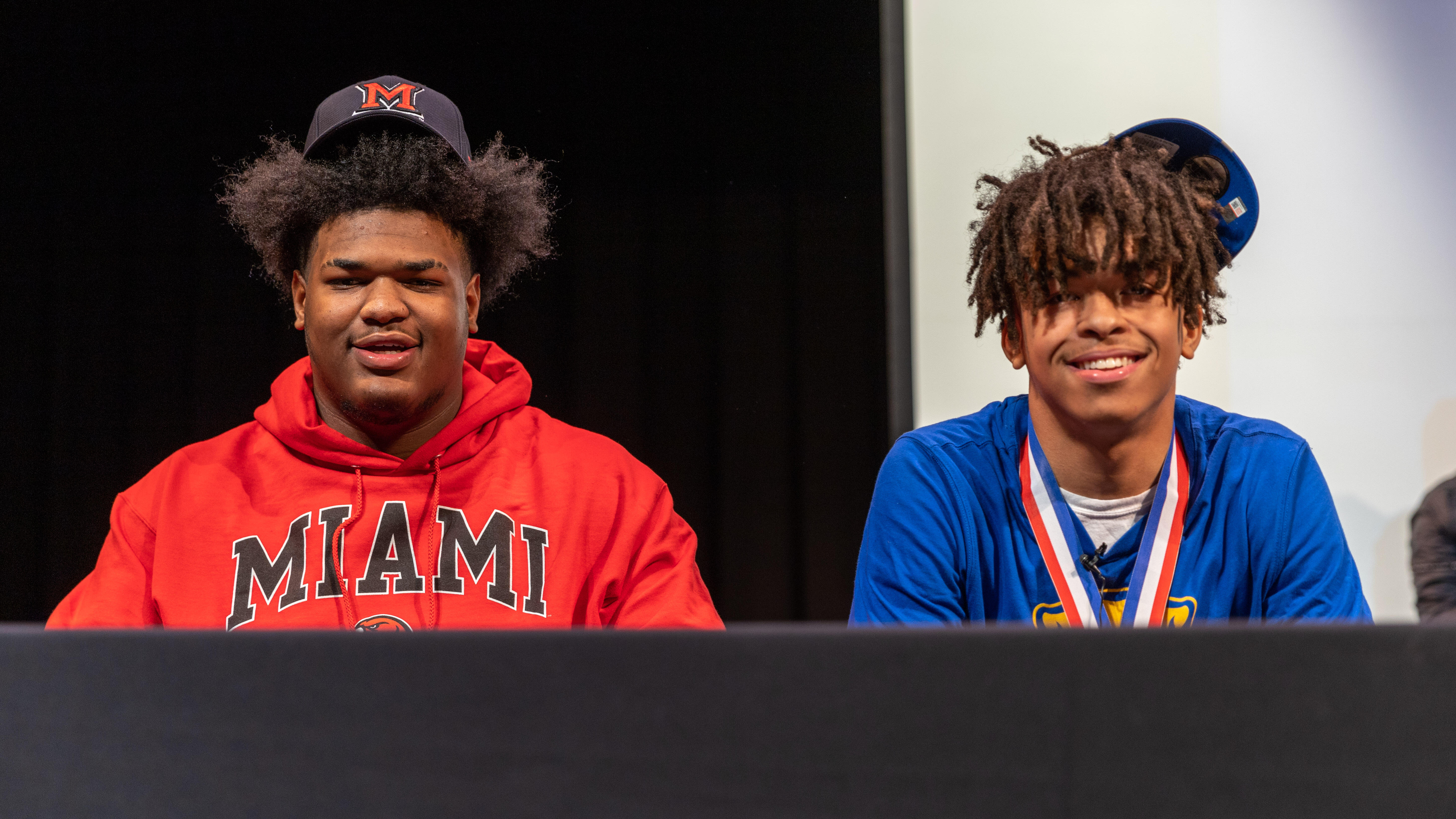 Greg Smith and Cruce Brookins pose for a picture seated at a table wearing their respective college school colors.