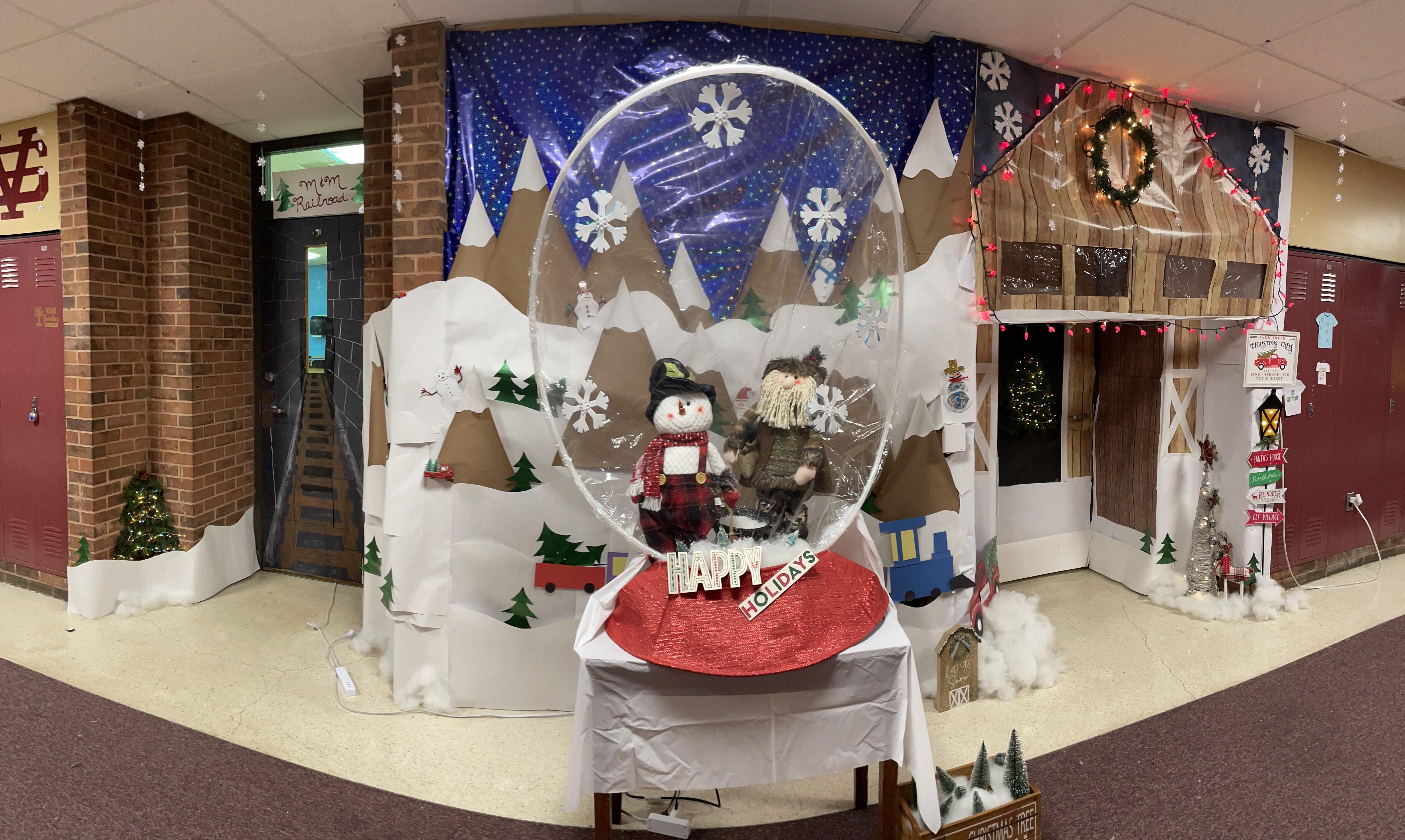 Two classroom doors are decorated to celebrate the holiday season. There is a giant piece of clear, circular plastic in front of them to make it look like a snowglobe.