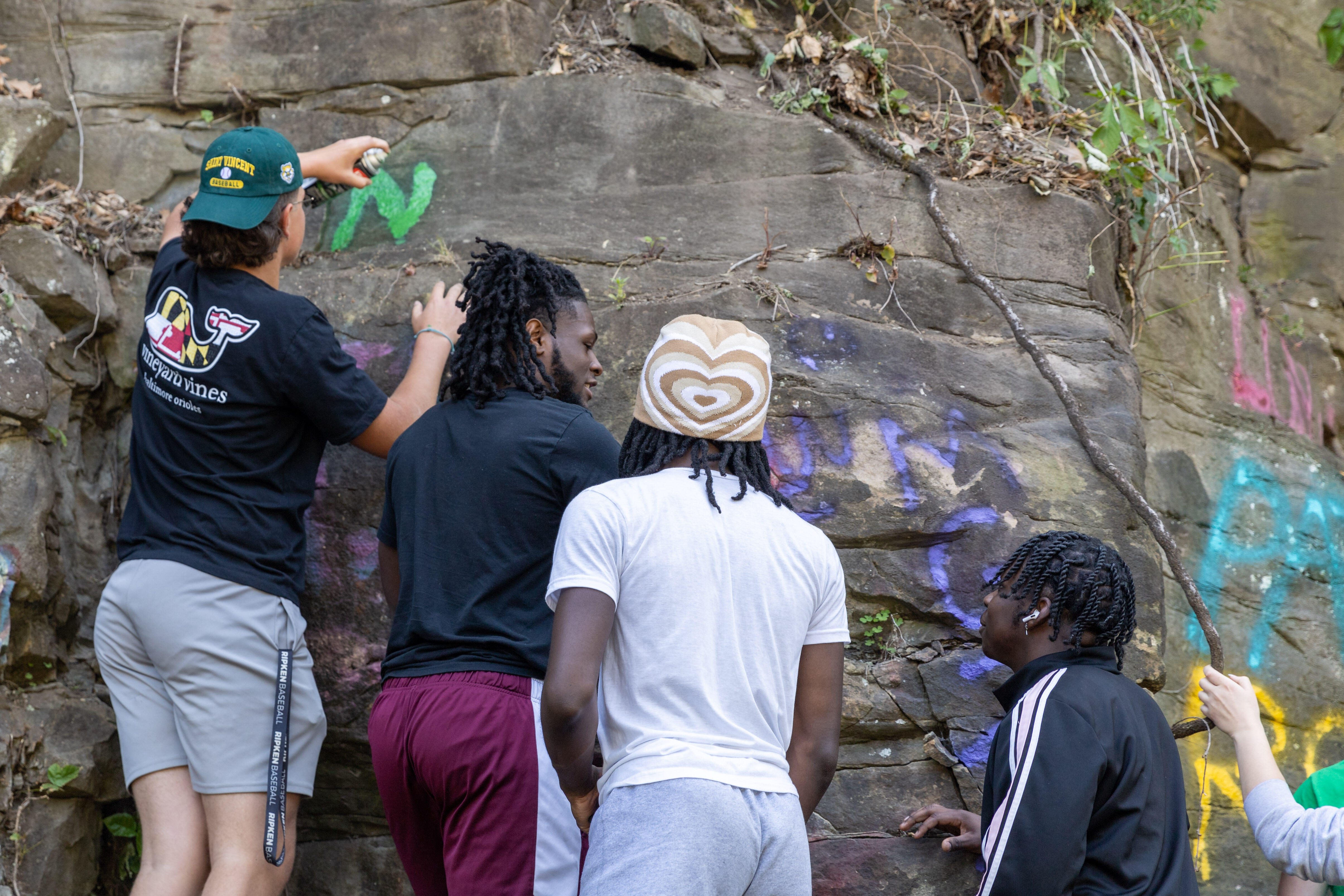 Students paint names on a rock wall