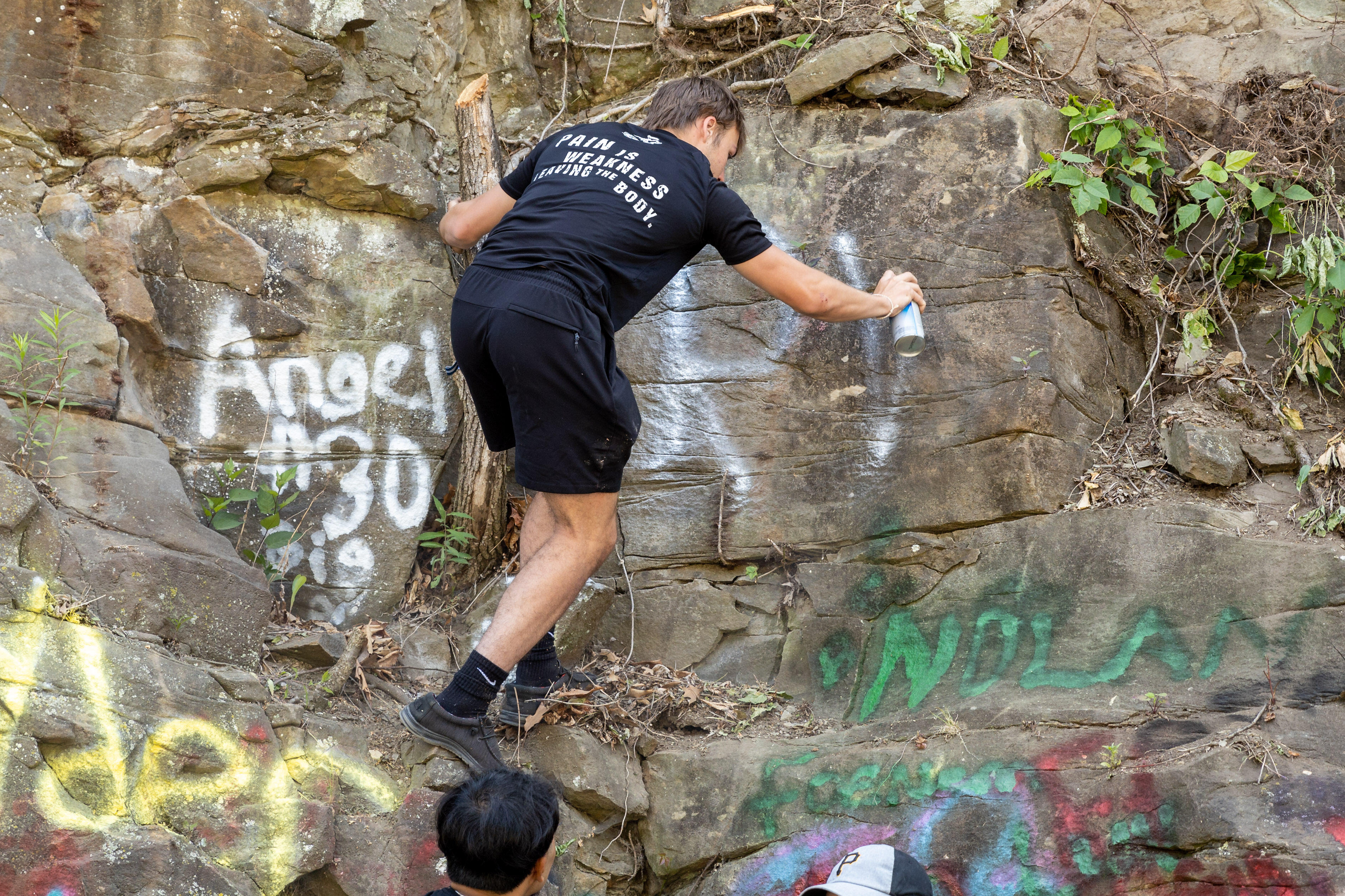 A student climbs a rock wall to paint his initials