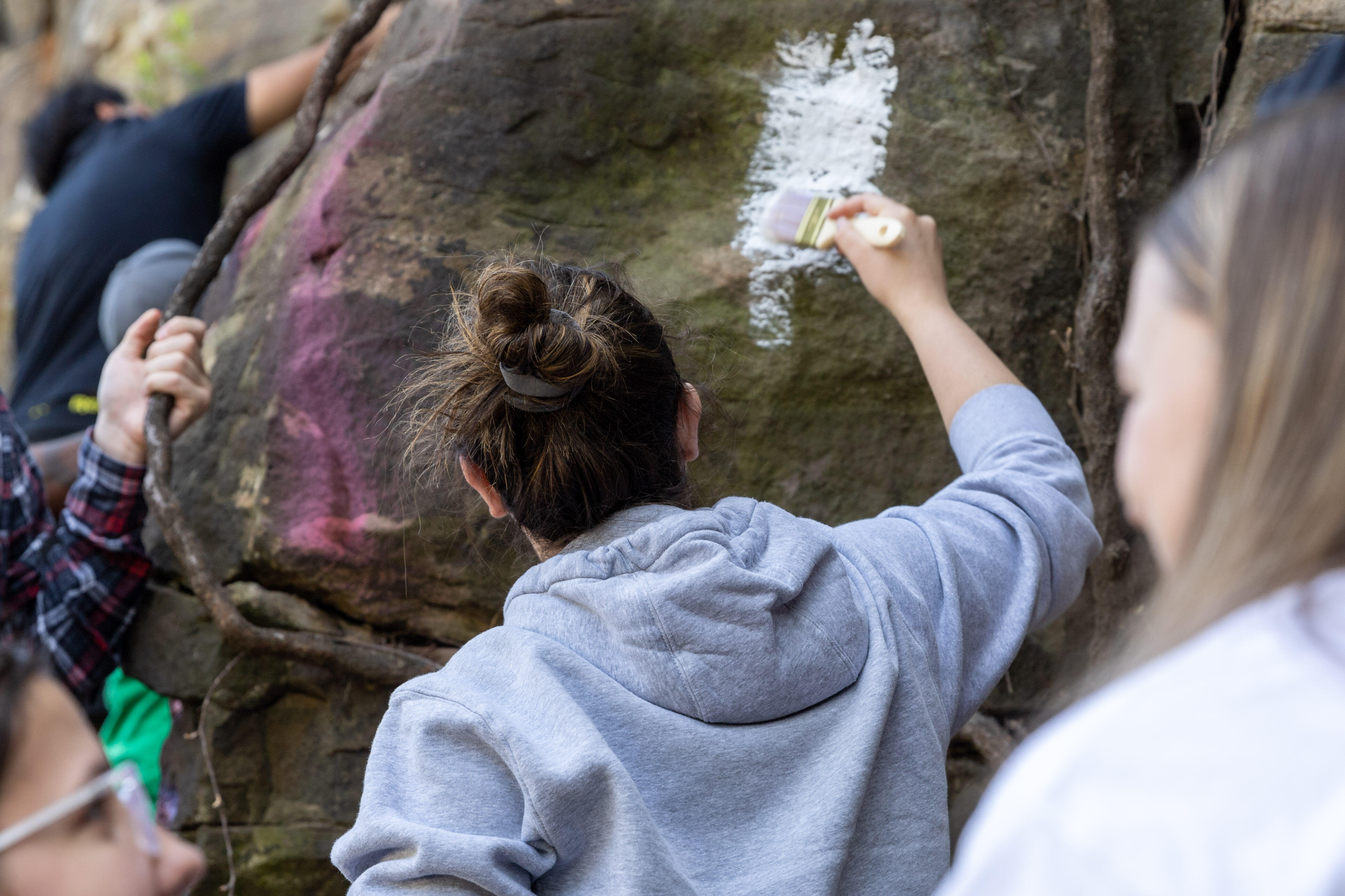 A student paints a rock wall
