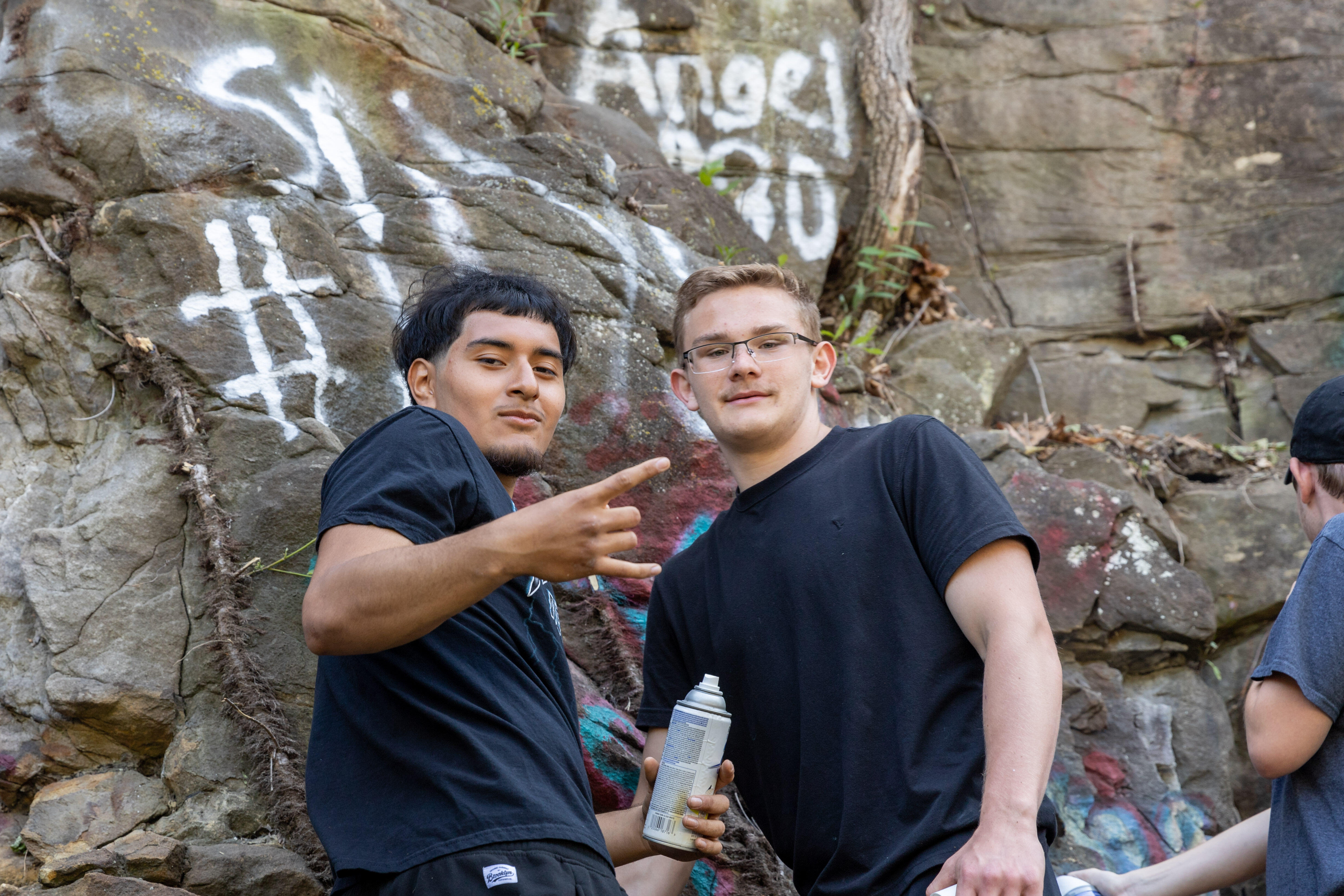 Two students pose for a photo while painting a rock wall