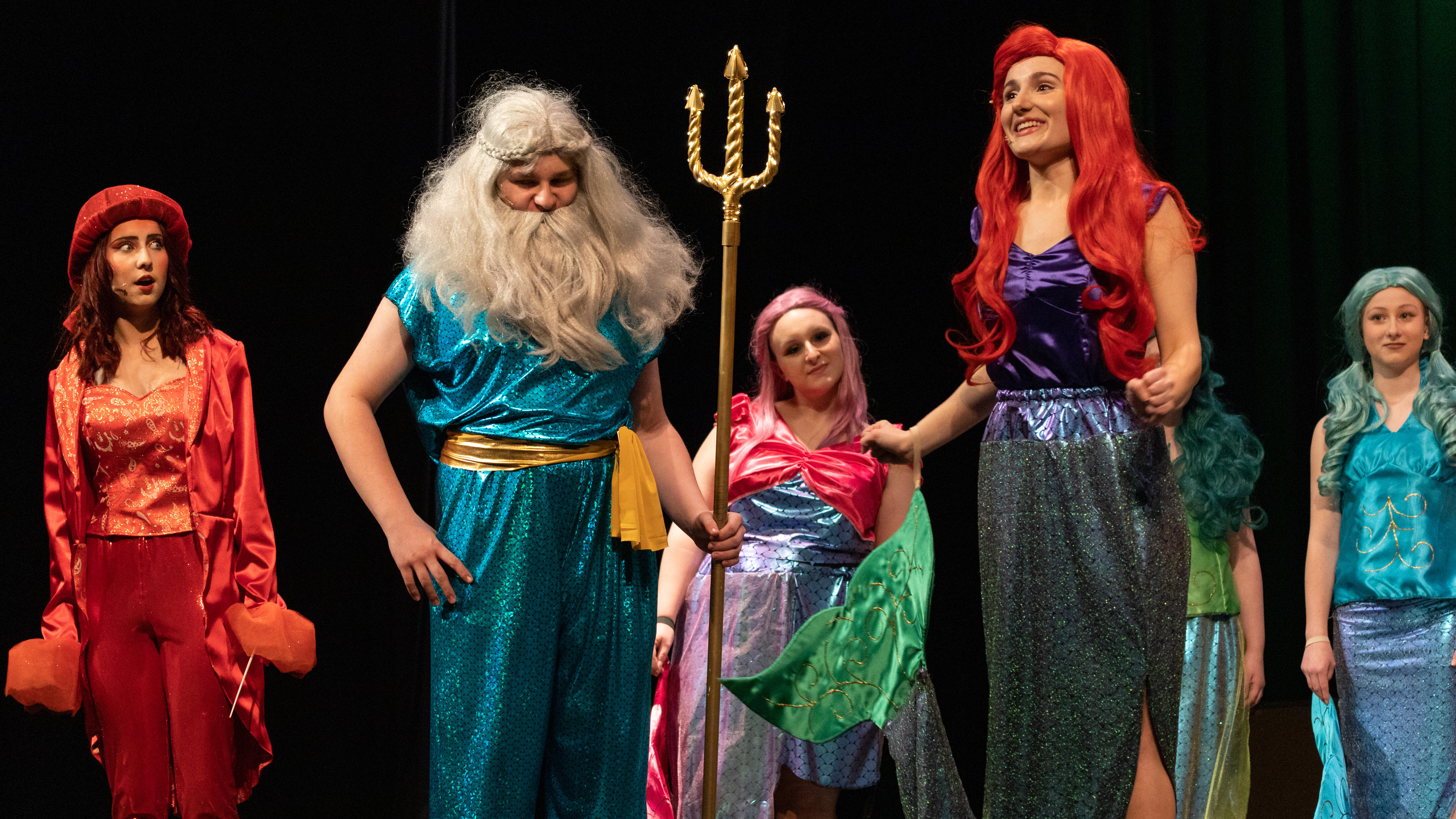 A scene from The Little Mermaid, as Ariel speaks with King Triton and Sebastian as the ensemble looks on behind them on stage