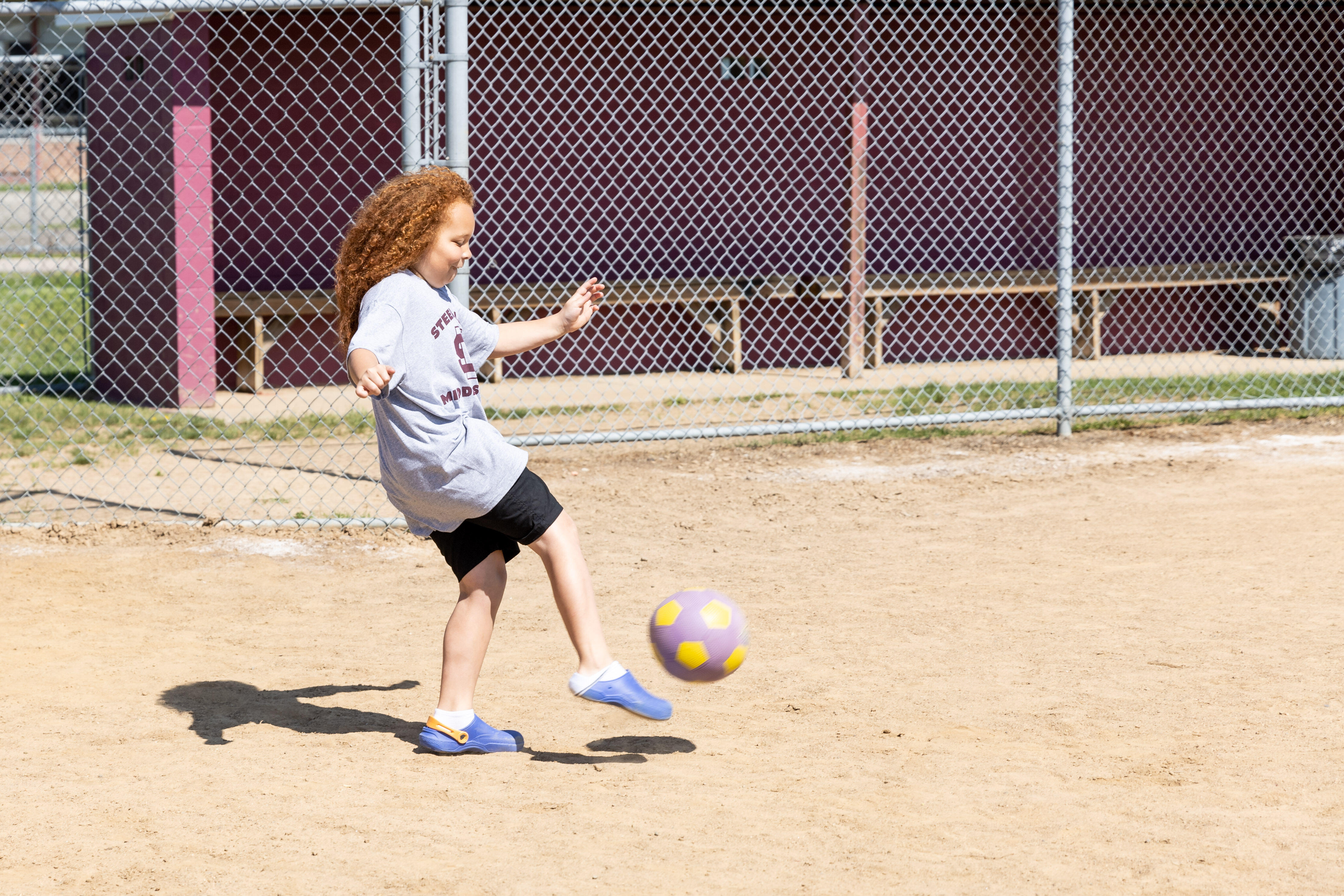 A student kicks a ball on a softball field while playing kickball