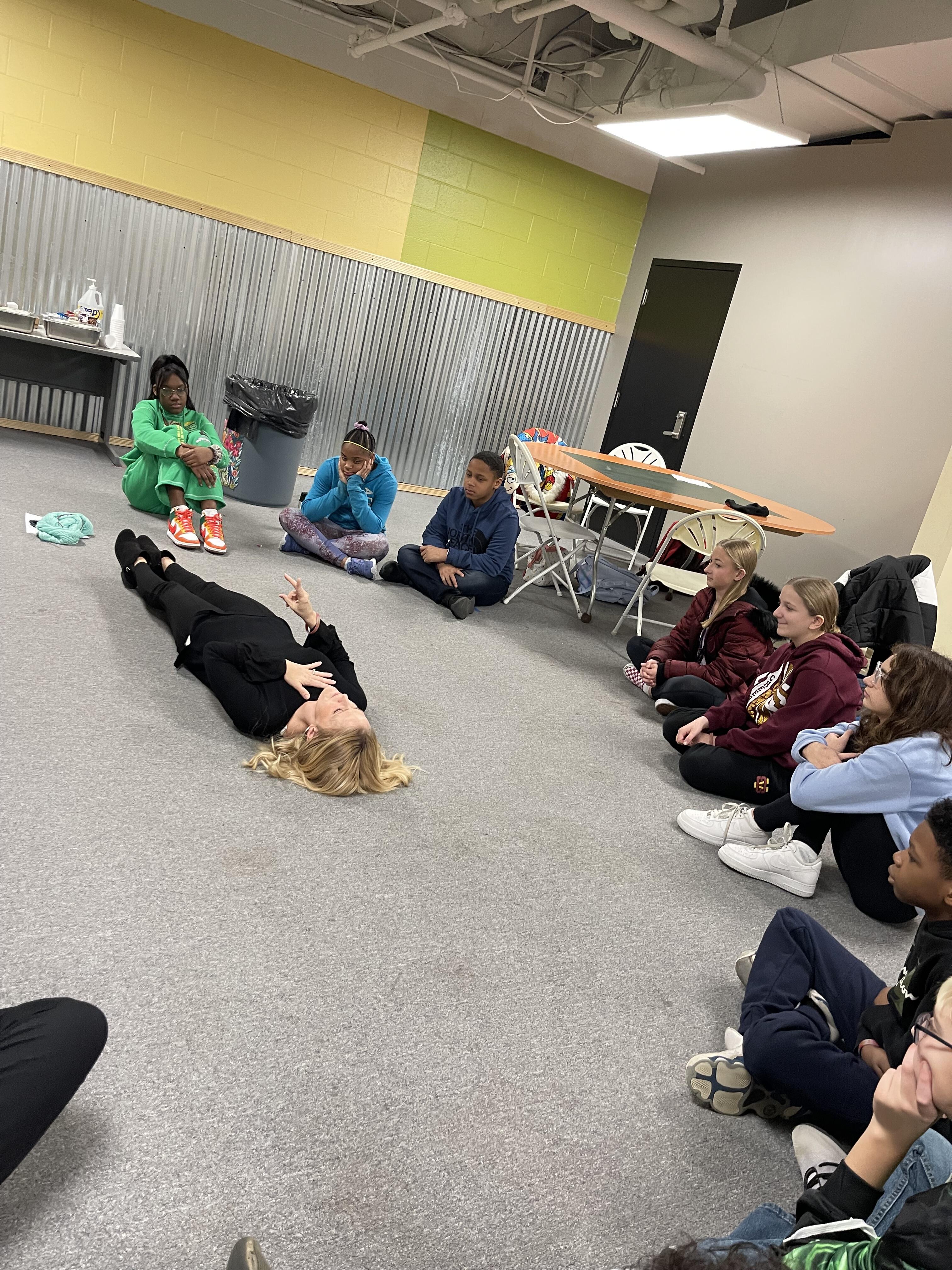 Students sit in a circle as part of a mental health workshop as an instructor lies on the ground teaching breathing techniques