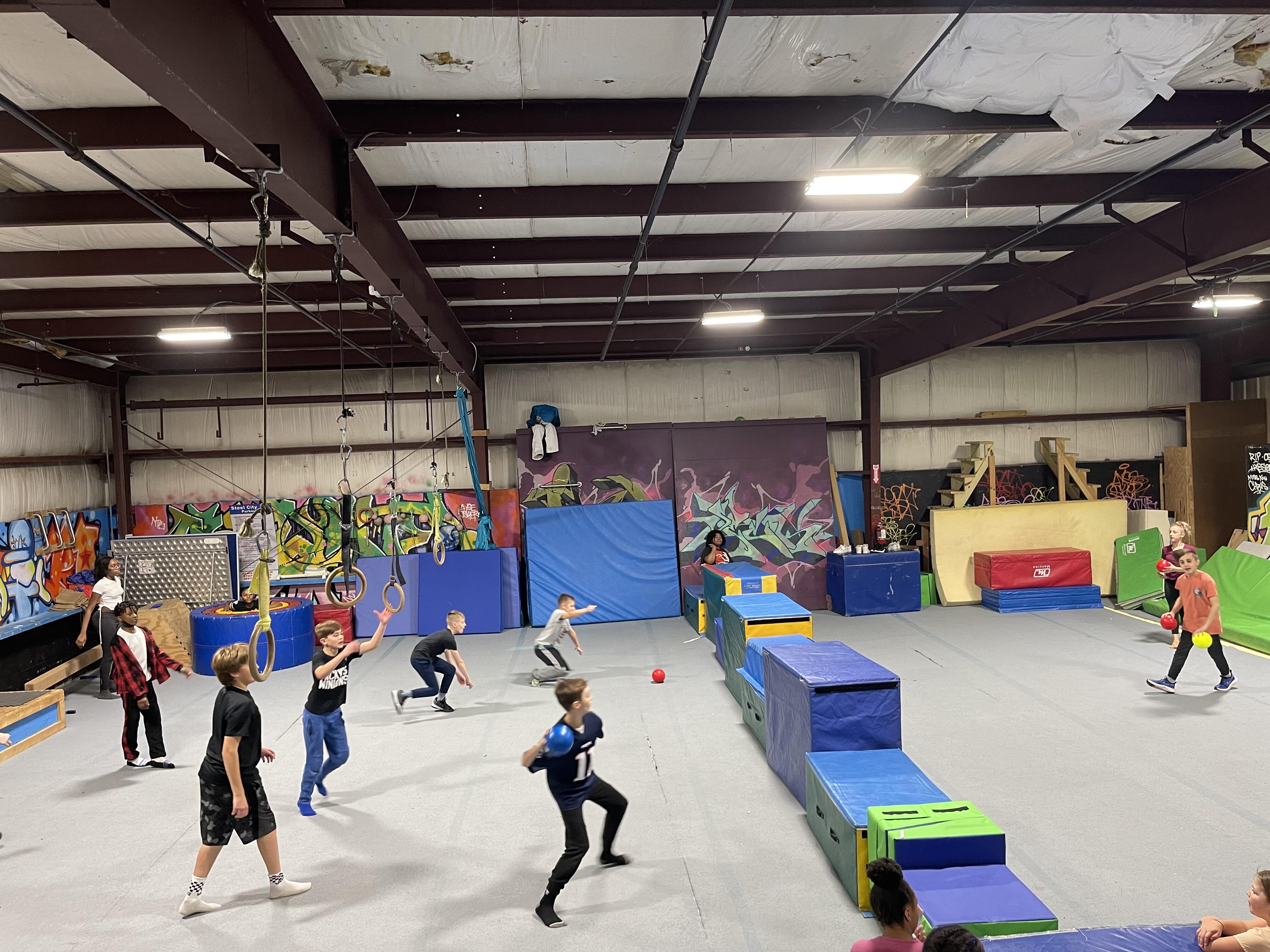Middle school students play dodgeball in a warehouse filled with trampolines and padding