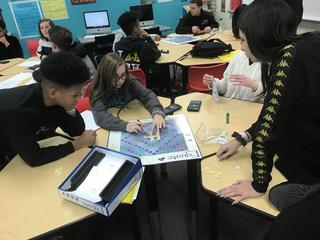 Student pointing at word on board game while others collaborate