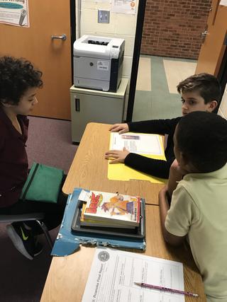 Three students discussing around a yellow folder