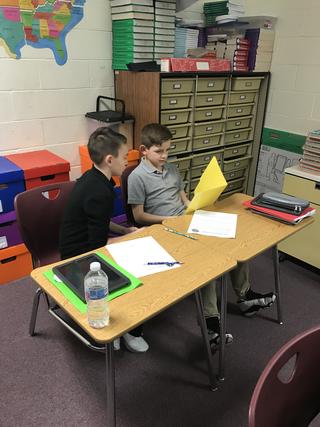 One student holds open yellow folder while both look at it