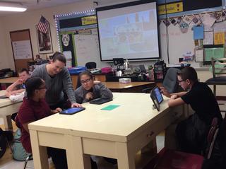 Teacher talks with students working on tablets at table