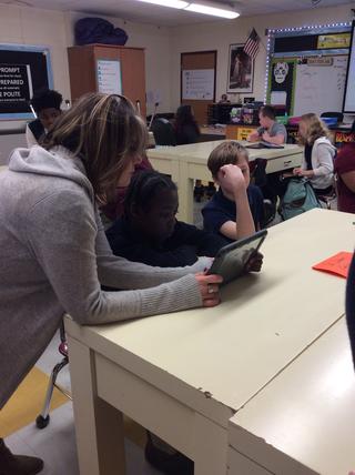 Teachers works with one student on tablet while other one looks on