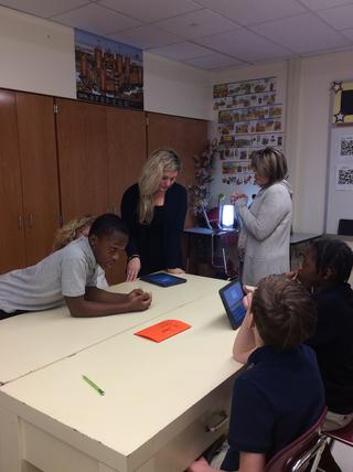 Teachers and students work with technology around a desk
